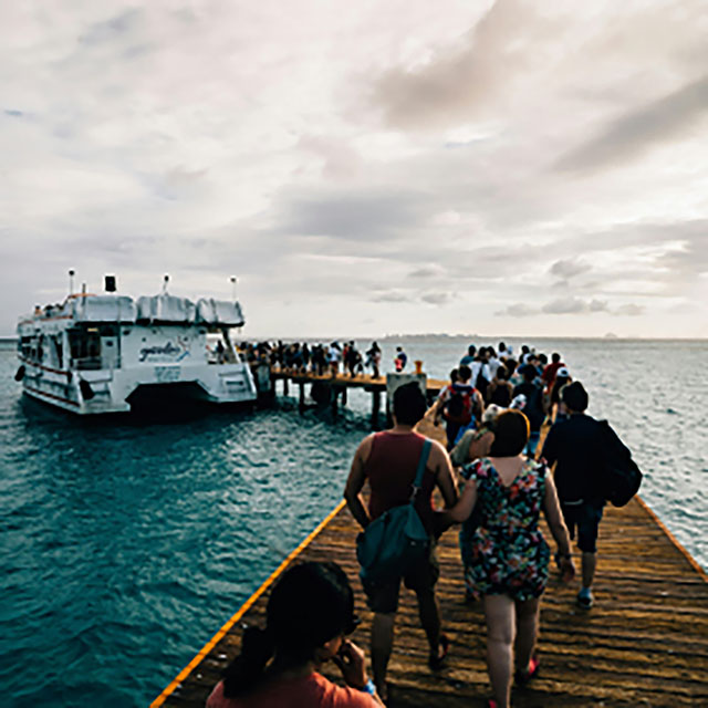 A group of people walking on a pier to a pontoon boat waiting on the lake