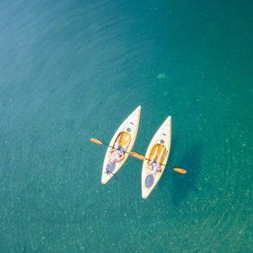 Birds-eye image of two canoes and two people paddling on blue water